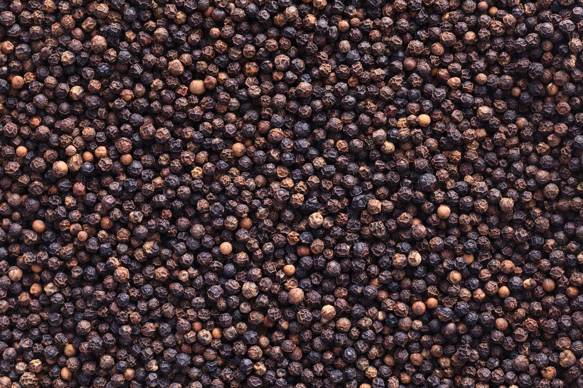 Close-up of dark brown peppercorns densely packed together as a background texture
